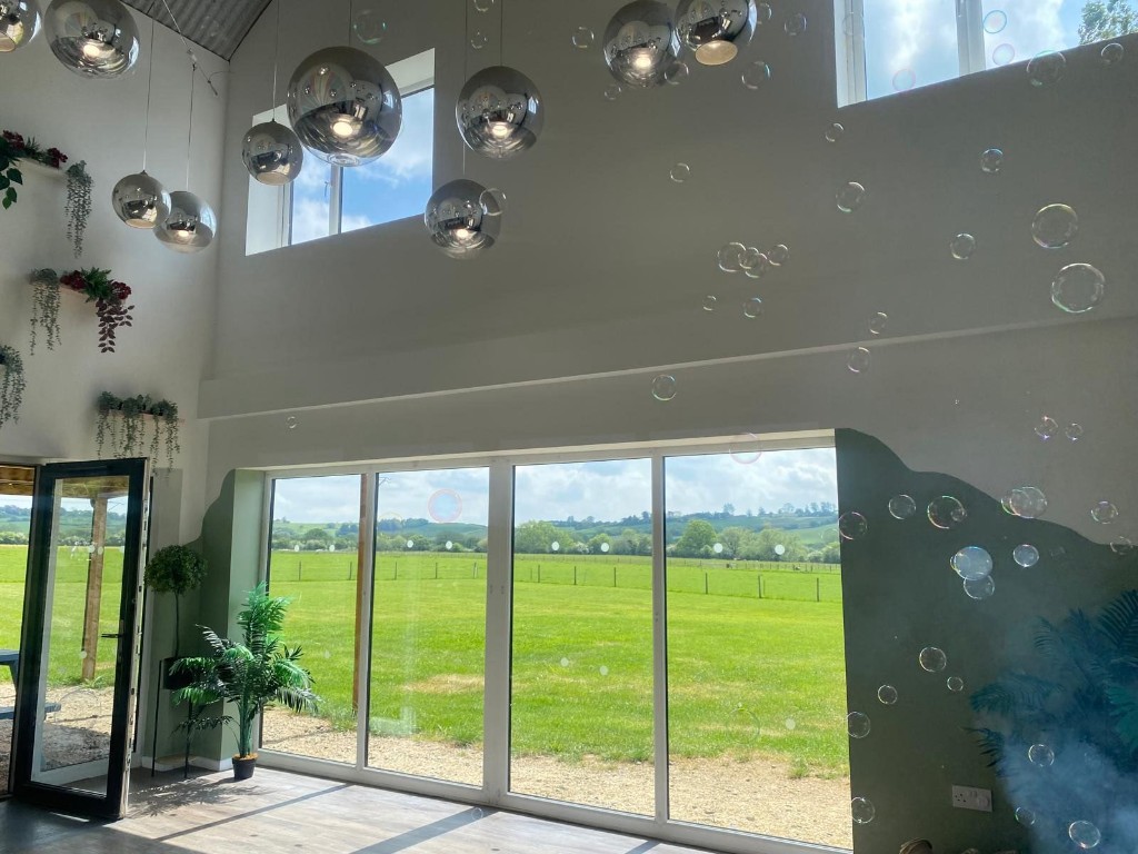 Bright interior with spherical pendant lighting, greenery and panoramic windows opening onto rolling countryside.